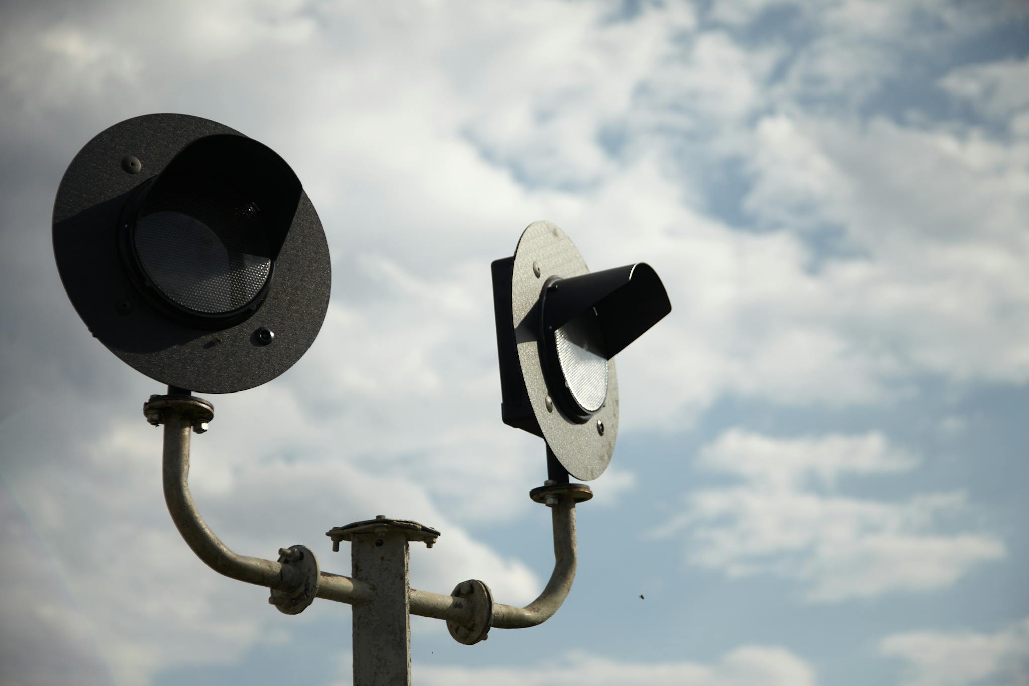 Detailed view of railway signal lights against a blue cloudy sky, showcasing transportation technology.